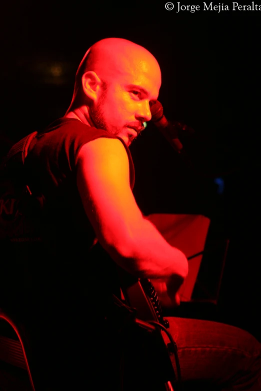 man sitting down while playing a guitar on a black background