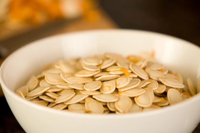a white bowl full of pumpkin seeds on a wooden table