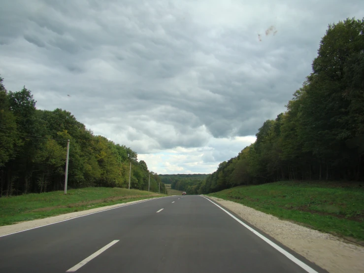 an empty road going through the woods under dark clouds