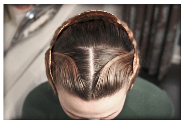 a person with long hair sitting at the head of a person wearing a basket like thing