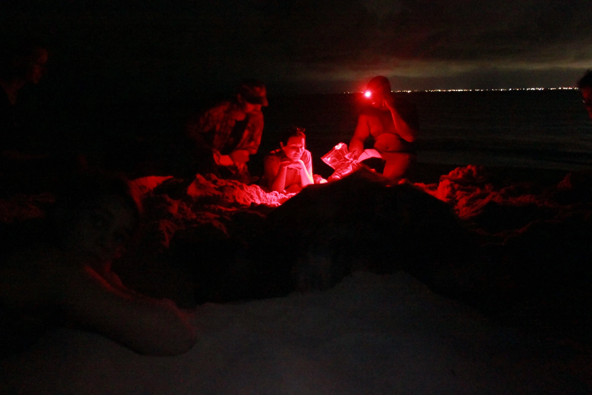 people gathered near a campfire under a red light at night