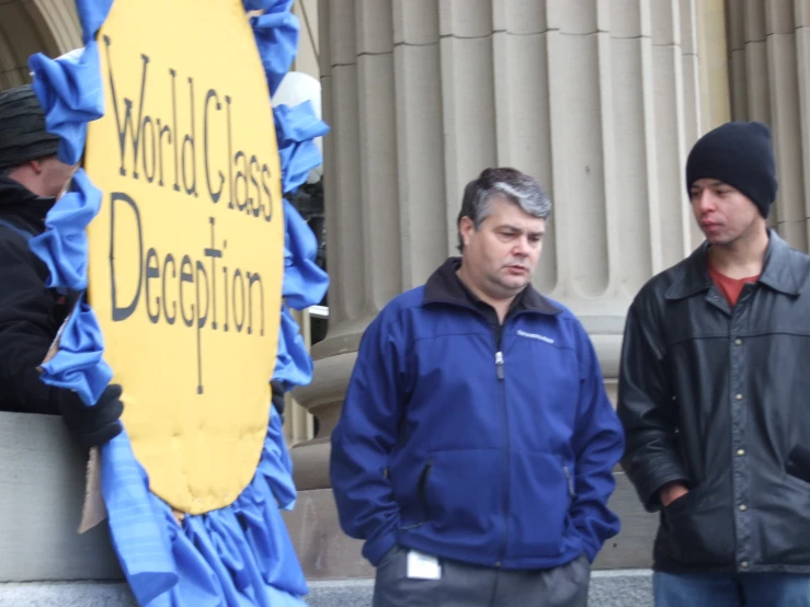 two men standing next to a sign that reads world class deception