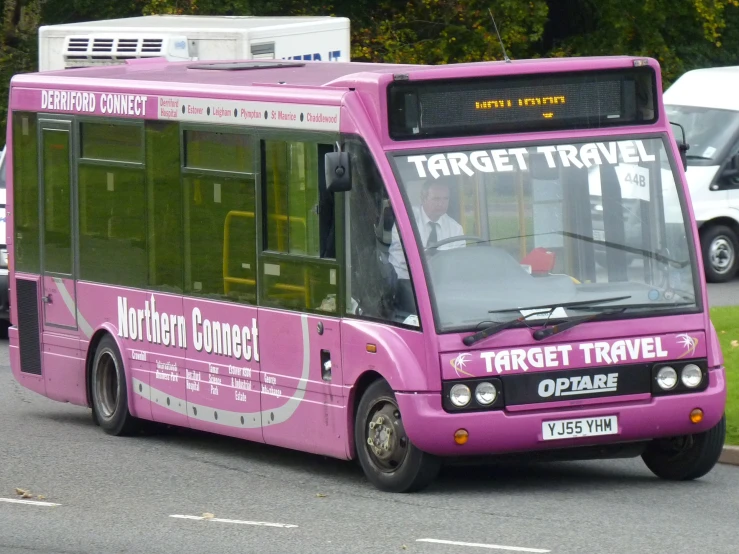 a pink commuter bus with words on it is in the road