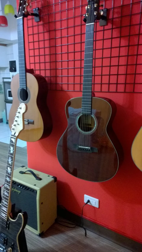 guitars hanging from a red wall near two amps