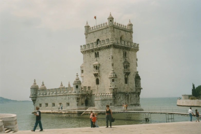 a group of people stand near the water outside a tower