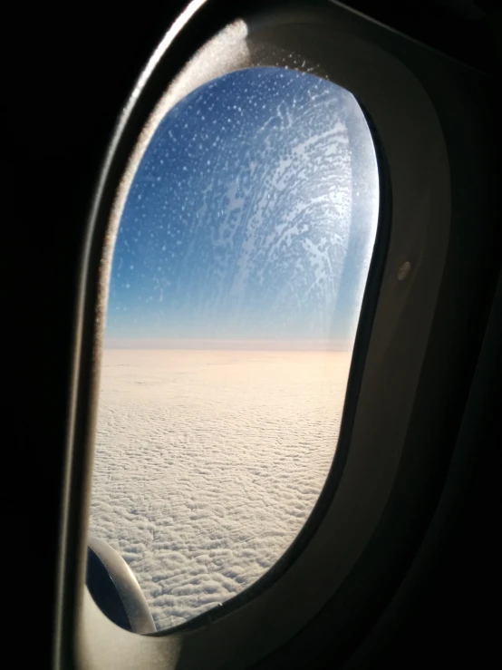 a window of an airplane over clouds under a blue sky