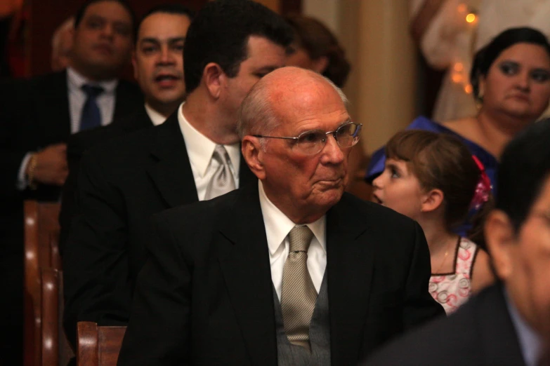 a man with a suit and tie sits in front of several people