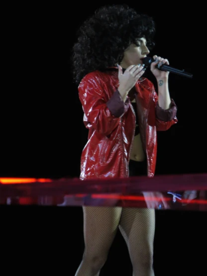 woman with curly hair singing into microphone at concert