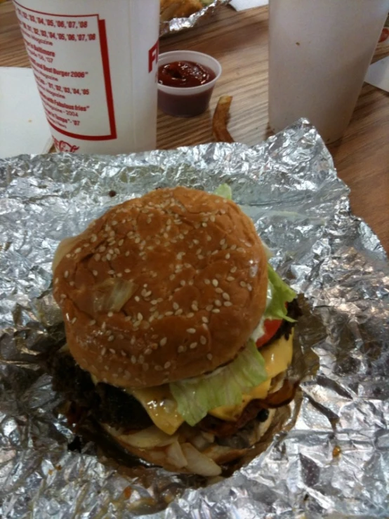 a hamburger covered in lettuce and onions sits on a foil wrapper