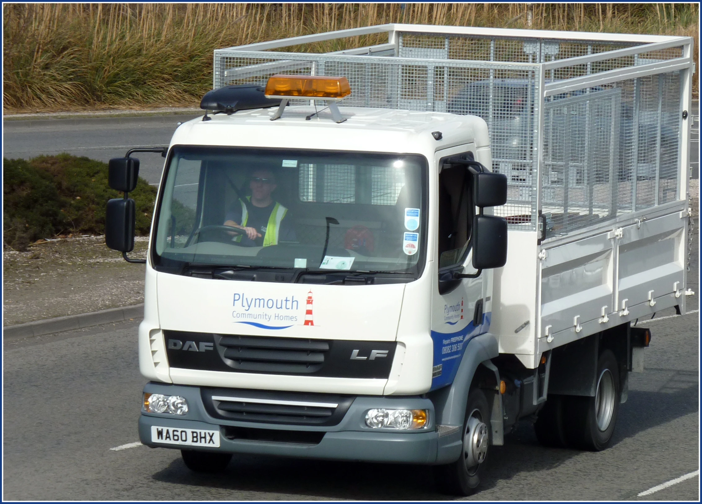 a white truck driving down a street with a man sitting in the driver seat