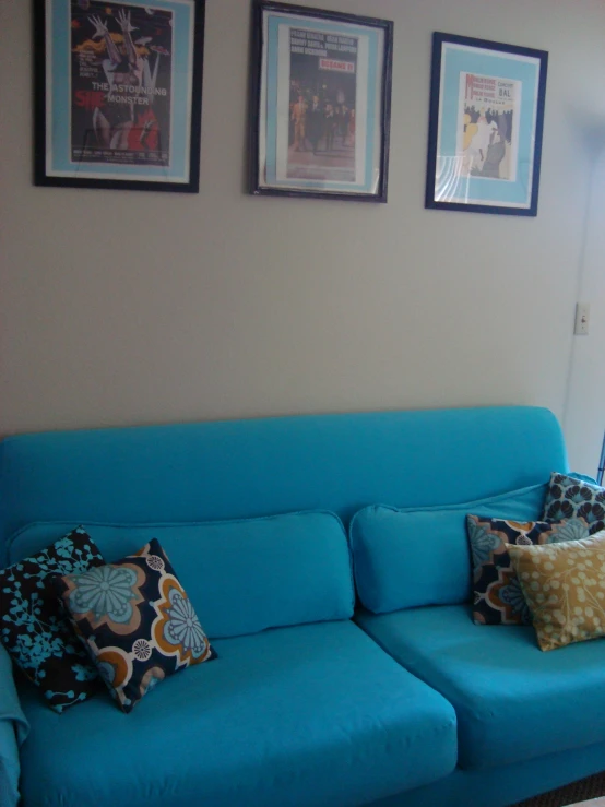 a blue couch in a living room with many framed pictures above it