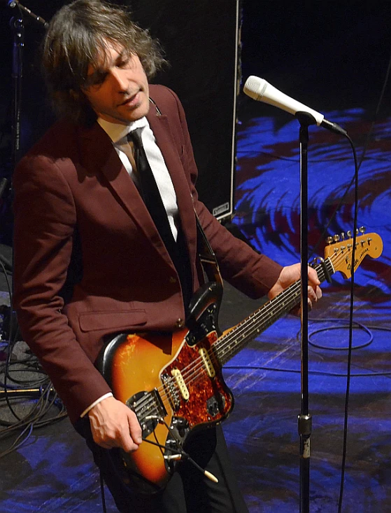 man in suit playing guitar and microphone near stage