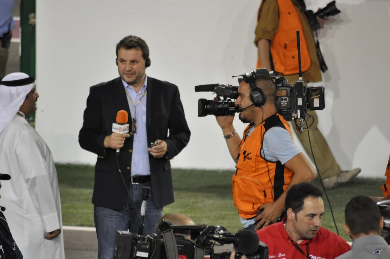 several cameras surrounding two men in orange safety vests