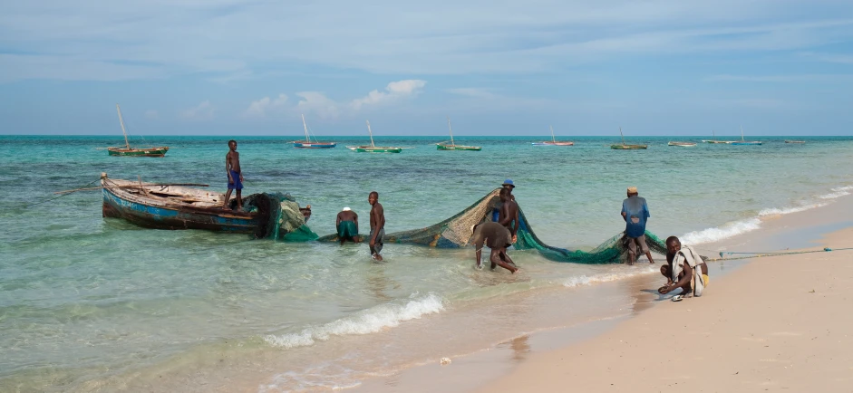 a few people near the water with boats in the background