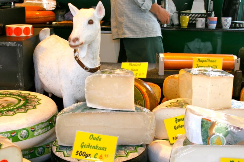 a cow stands in front of cheese that are for sale