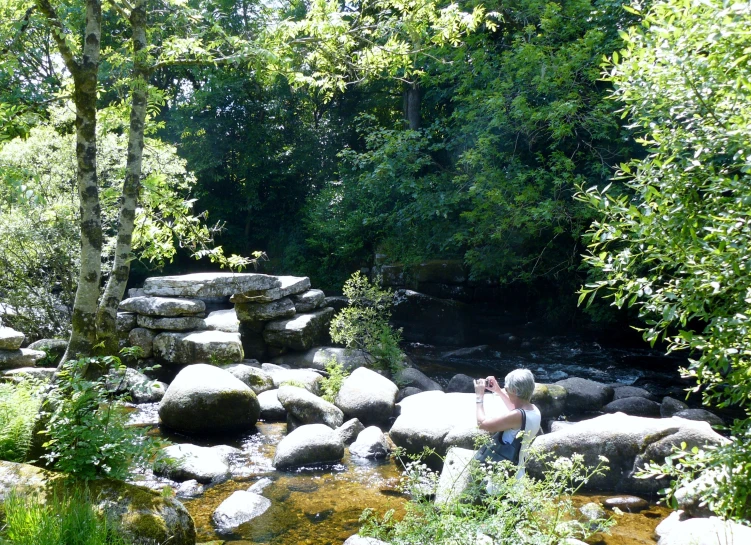 a man standing in the middle of a stream surrounded by rocks and a forest