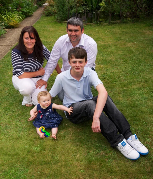 three people sitting in a grass yard with one holding a child