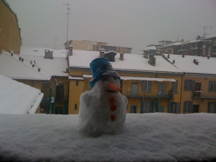 a snowman on the ground near a building with a snowstorm coming down