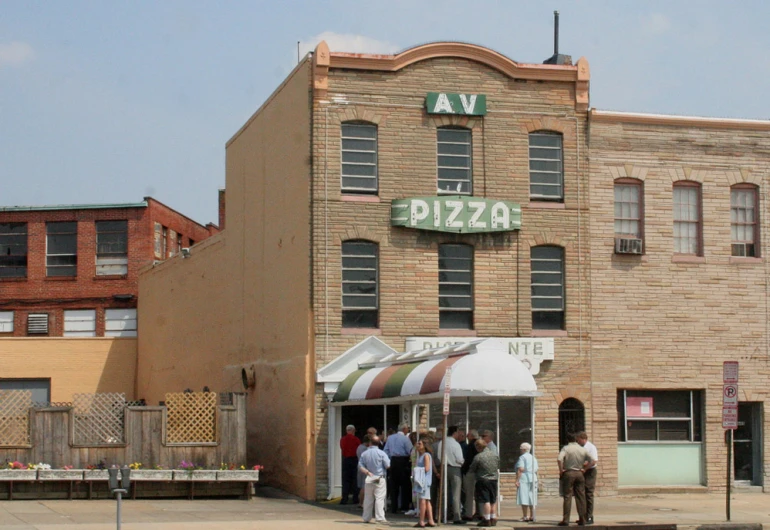 a group of people are standing in front of a brick pizza shop