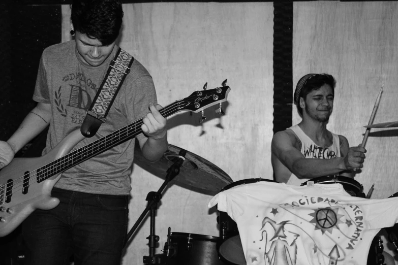 two men holding guitars and some drums while sitting on chairs