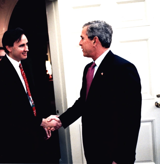 two men in suits shaking hands in front of the door