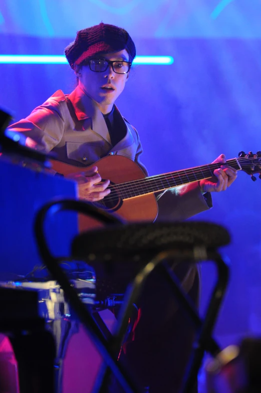 a man in glasses and a black hat is playing an acoustic guitar