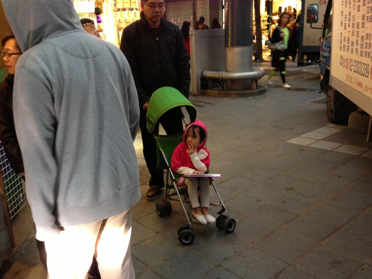 young child hing green stroller on street corner