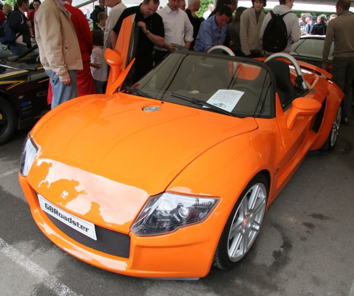 a orange car sitting on top of a street next to a crowd