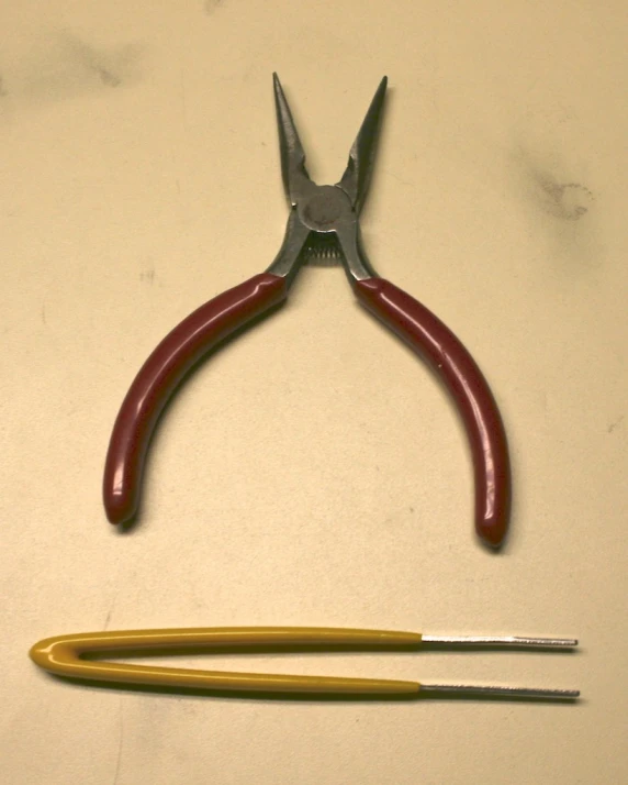 a pair of red handles with two yellow tips and a small wire cutter next to them
