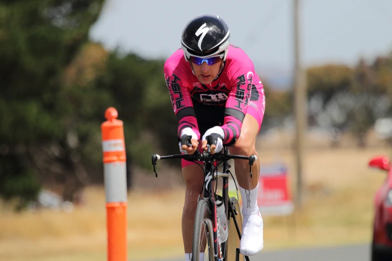 a male biker in a pink shirt and helmet riding his bicycle