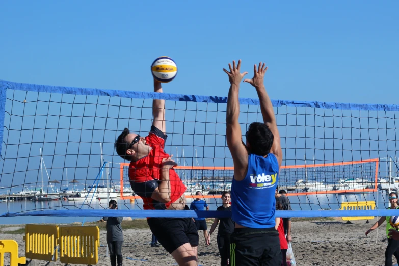 three men in blue shirts playing volleyball on the beach