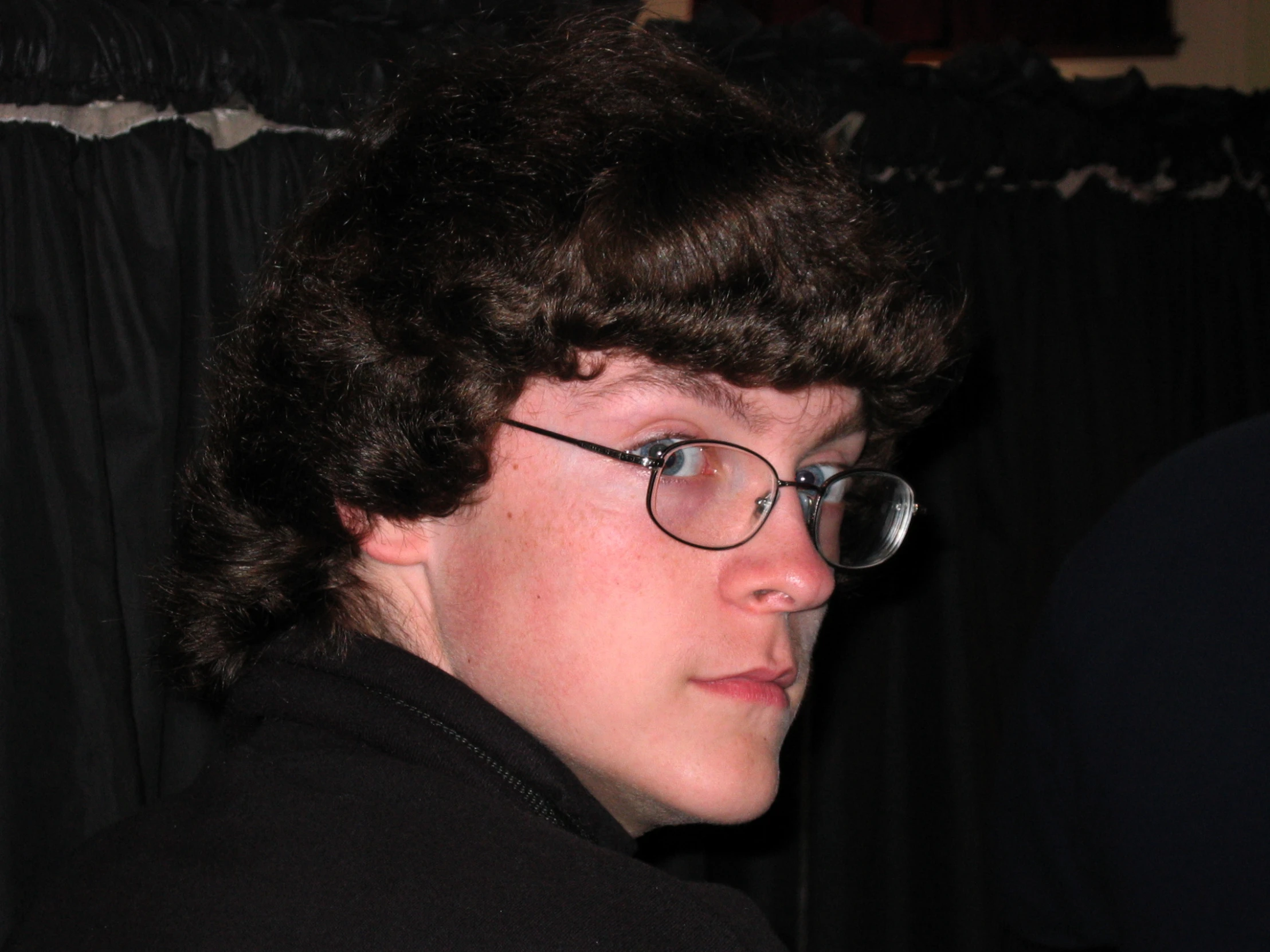 a young man in glasses and jacket in front of black curtain