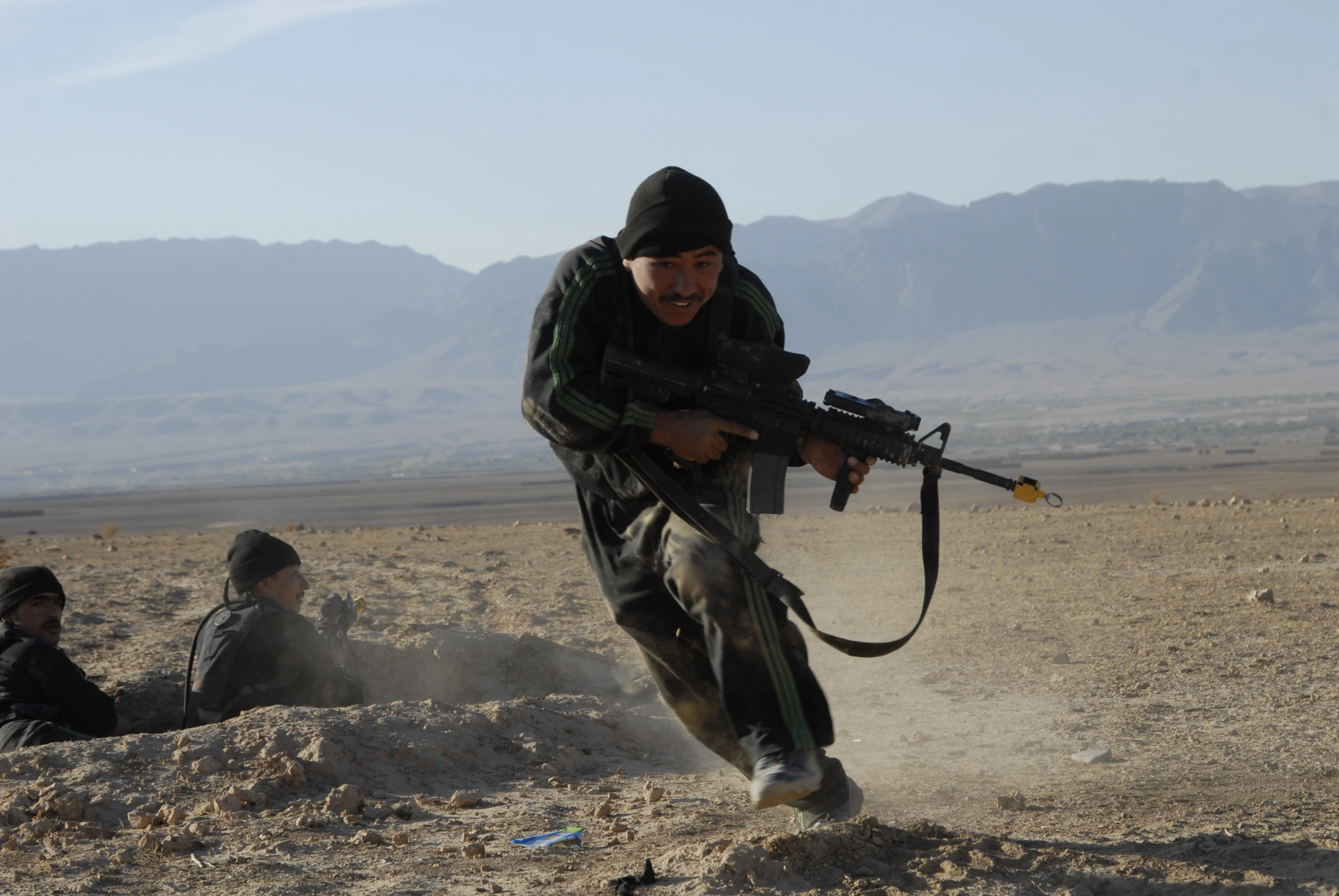 a man holds a gun over his shoulder as he sits on the ground next to another man