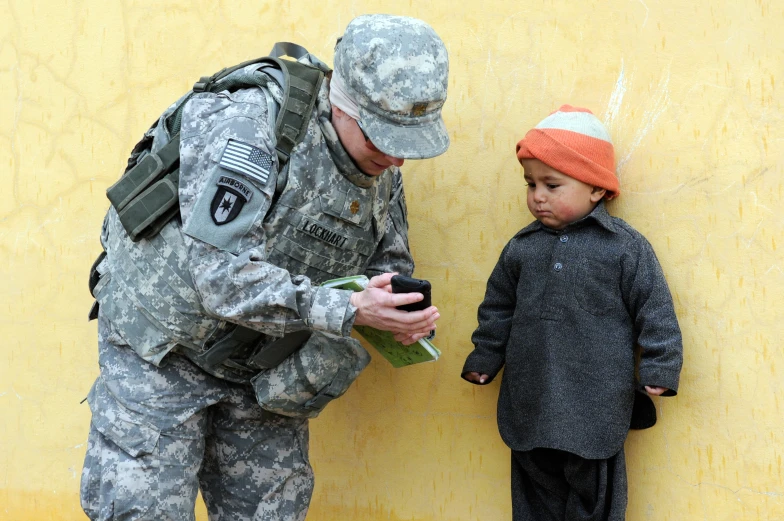 a soldier is holding a phone to a small child