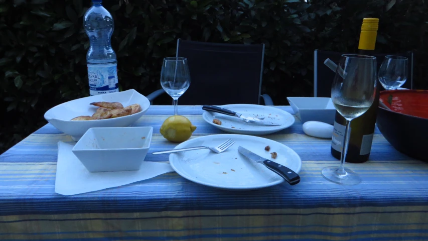 plates and bowls with food and wine sit on a table outside