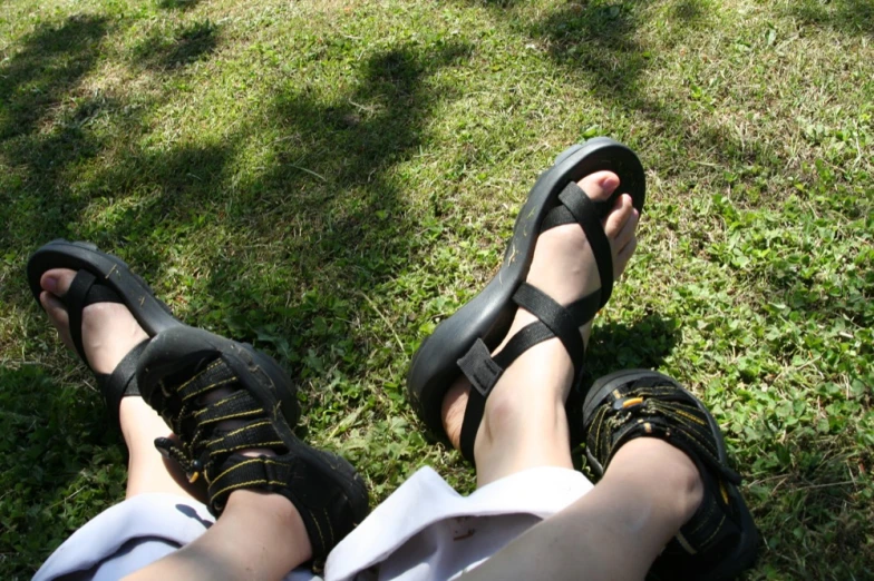 a person sitting on the grass with their feet in a pair of sandals