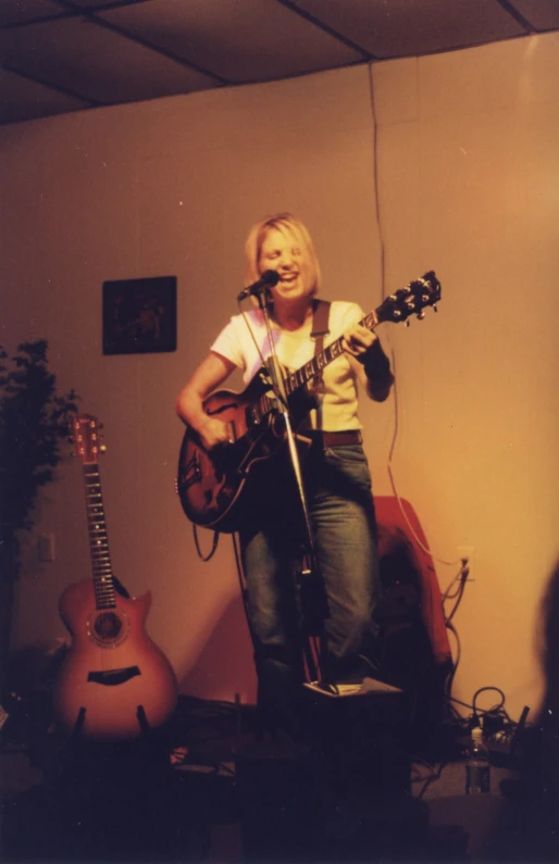 a woman playing a guitar in front of some guitars