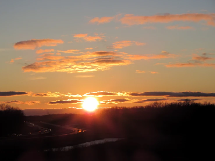 the sun sets over a rural landscape near a body of water