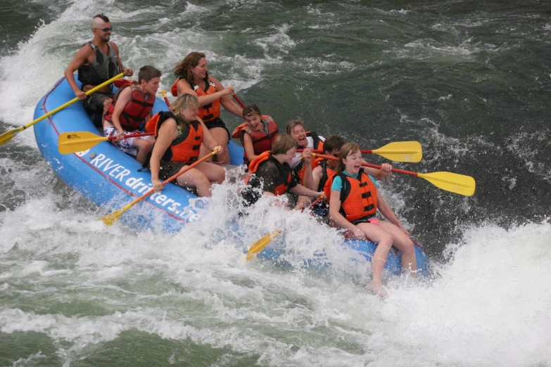 a group of young people paddling a blue raft down rapids