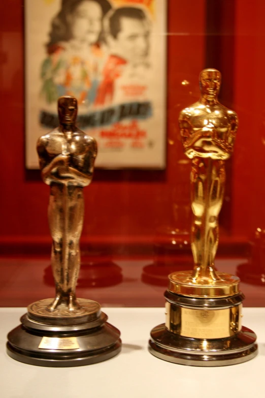 two oscar statues displayed in front of a red wall