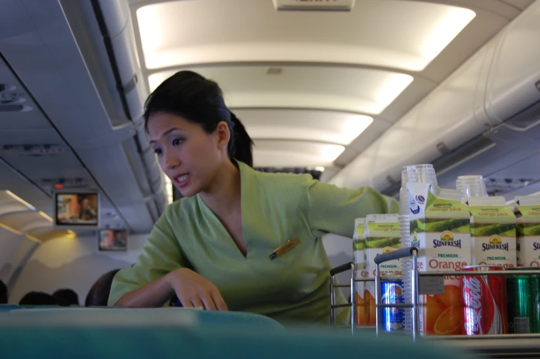 a woman sitting down in an airplane with a shelf full of drinks