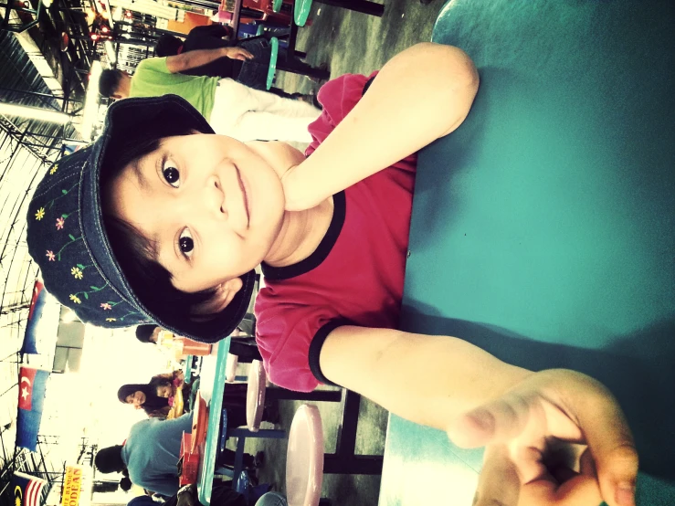 a little boy sitting at a green table wearing a hat