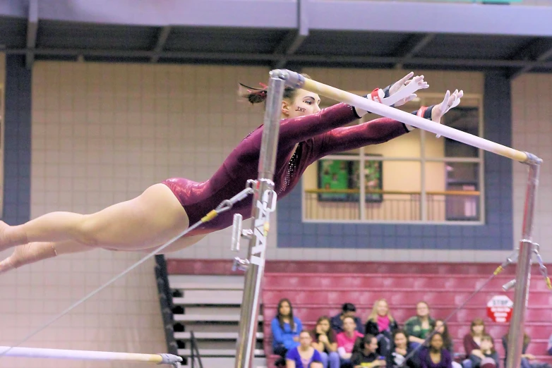 woman in maroon doing a stunt on a high bar