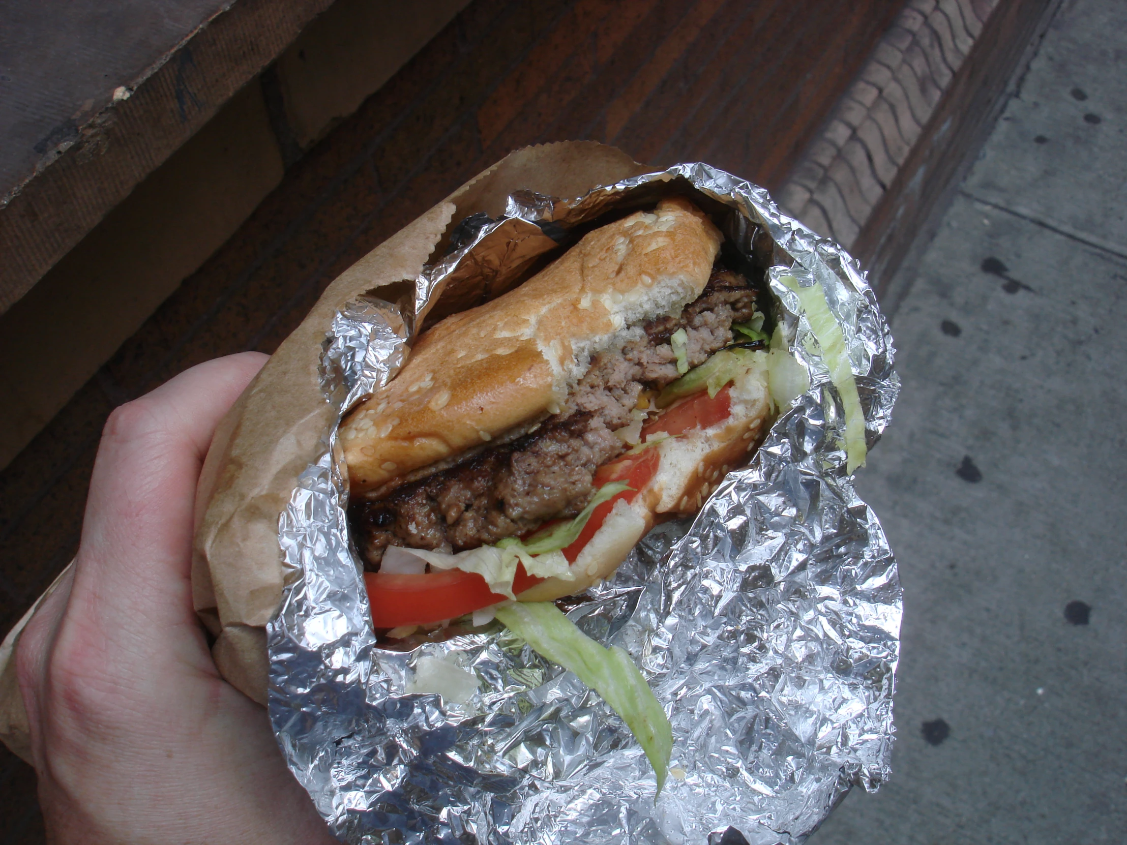 someone holding a large hamburger on some foil