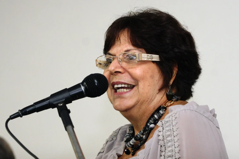 an older woman wearing glasses in front of a microphone