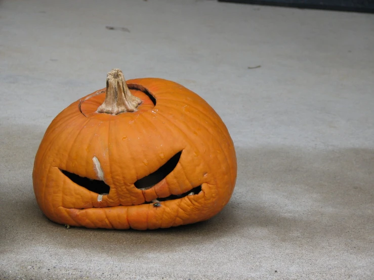 a small pumpkin with a jack - o - lantern face in the middle of cement