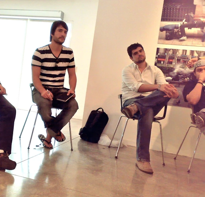 three men sitting in chairs with luggage talking