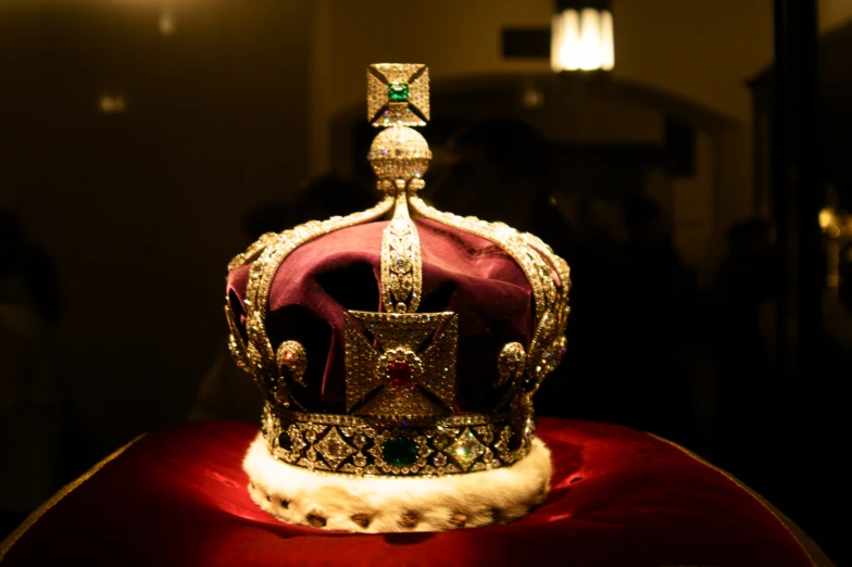 a shiny gold crown sits on top of a red cushion