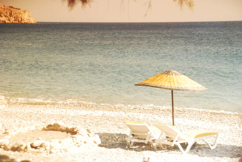 two lawn chairs under an umbrella on the beach