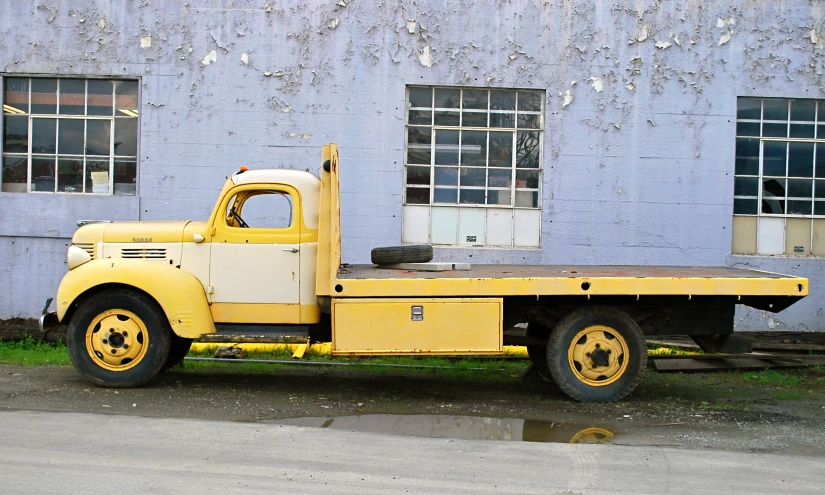 an old truck with a flat bed is parked in front of a building